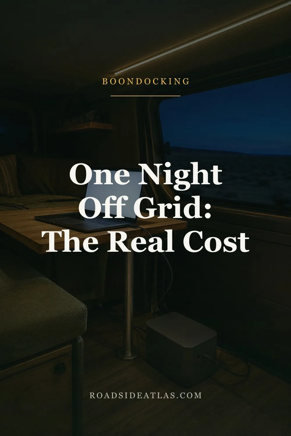 The interior of a campervan at night lit only by a warm LED strip along the ceiling, a laptop open on a wooden table and a matte grey battery box on the floor